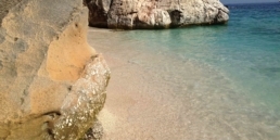 Atmosfera marina rilassante sulla spiaggia con rocce e acque cristalline, perfetta per musica e relax mare. Location ideale per eventi musicali sulla spiaggia.